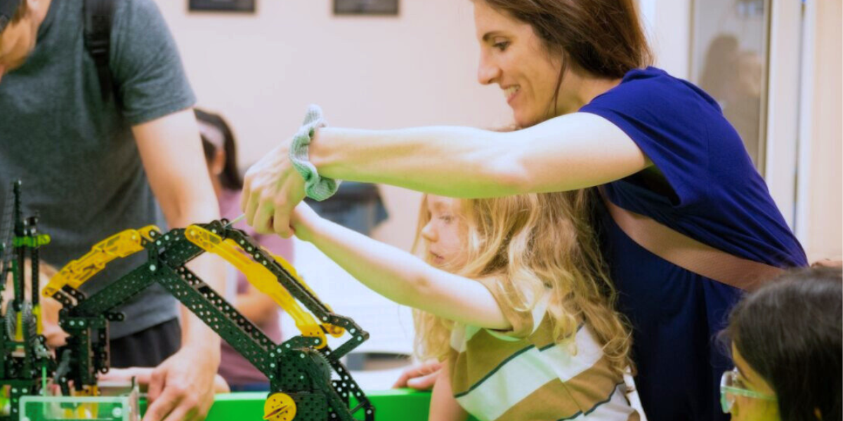 A parent and child work side by side to build a robot, sharing knowledge and enjoying a creative bonding moment. The project inspires curiosity and introduces engineering concepts in a supportive environment.