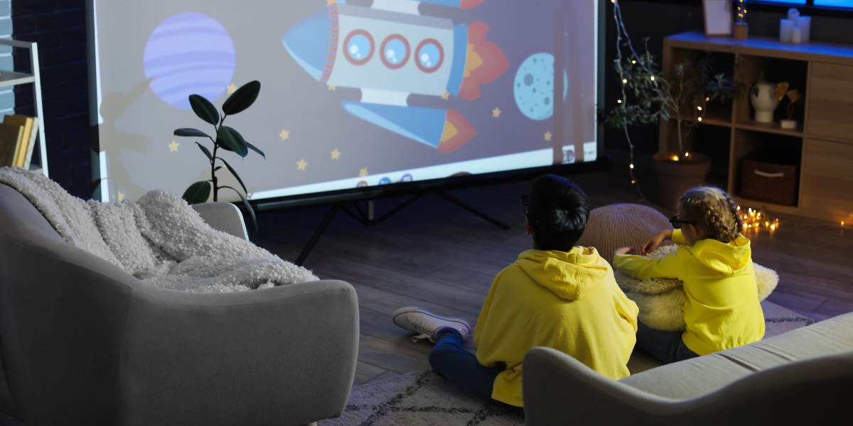 Two children in yellow hoodies sitting on the floor watching a colorful rocket and planet animation, getting excited about space through educational entertainment at home.