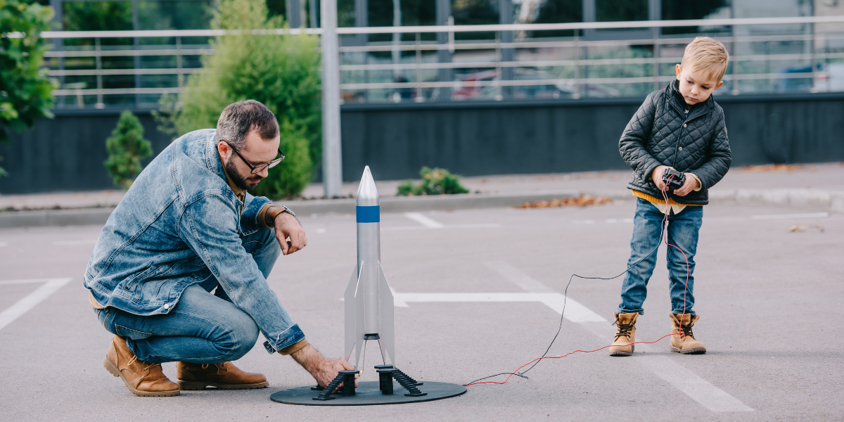 Father and son launching model rocket space experiment Father and young boy getting excited about space science while launching a model rocket in a parking lot, demonstrating hands-on learning about aerospace principles.