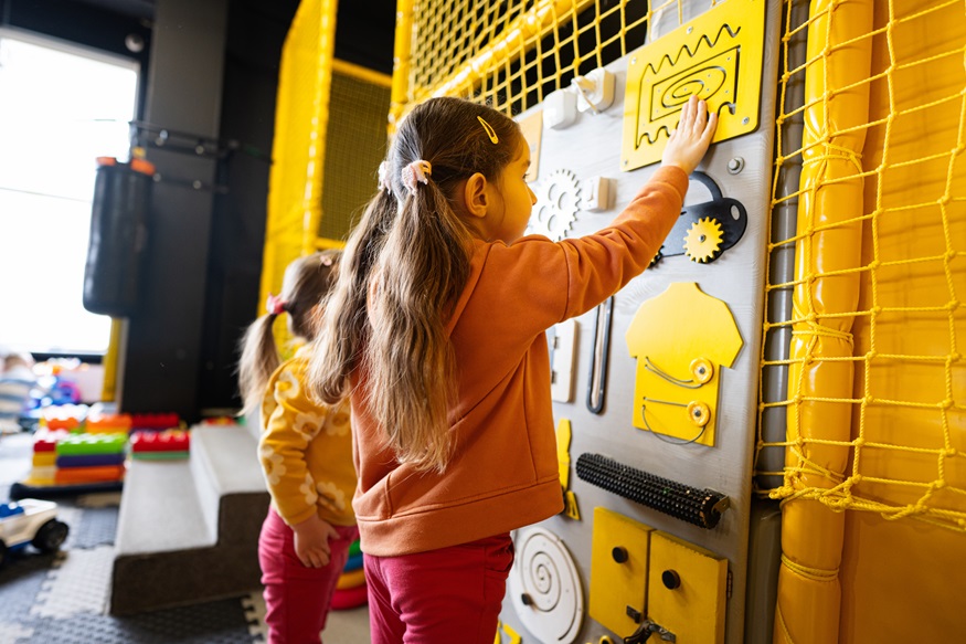 Two sisters playing with busy board at kids play center.